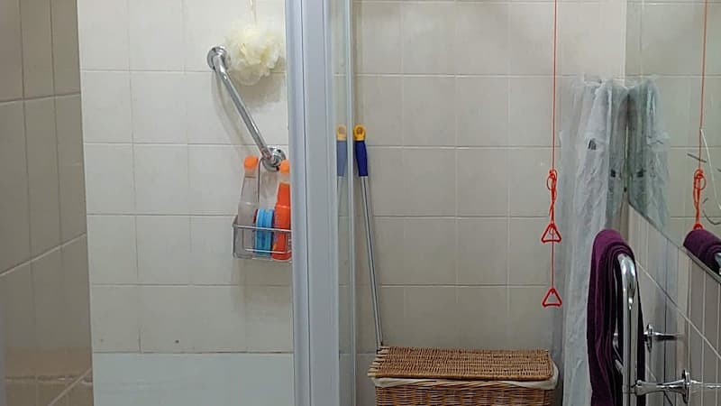 messy bathroom with handrails in shower