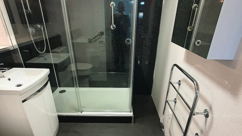 Black bathroom shower with handrails and a shite sink and wall