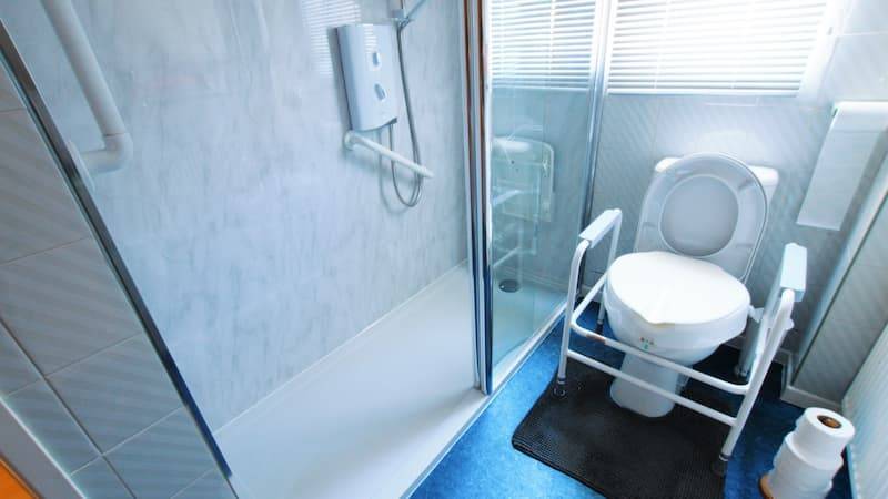 Blue bathroom with walk in shower with seat and handrails and a supported toilet