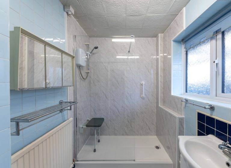 Clean bathroom with big walk in shower with handrail and seat